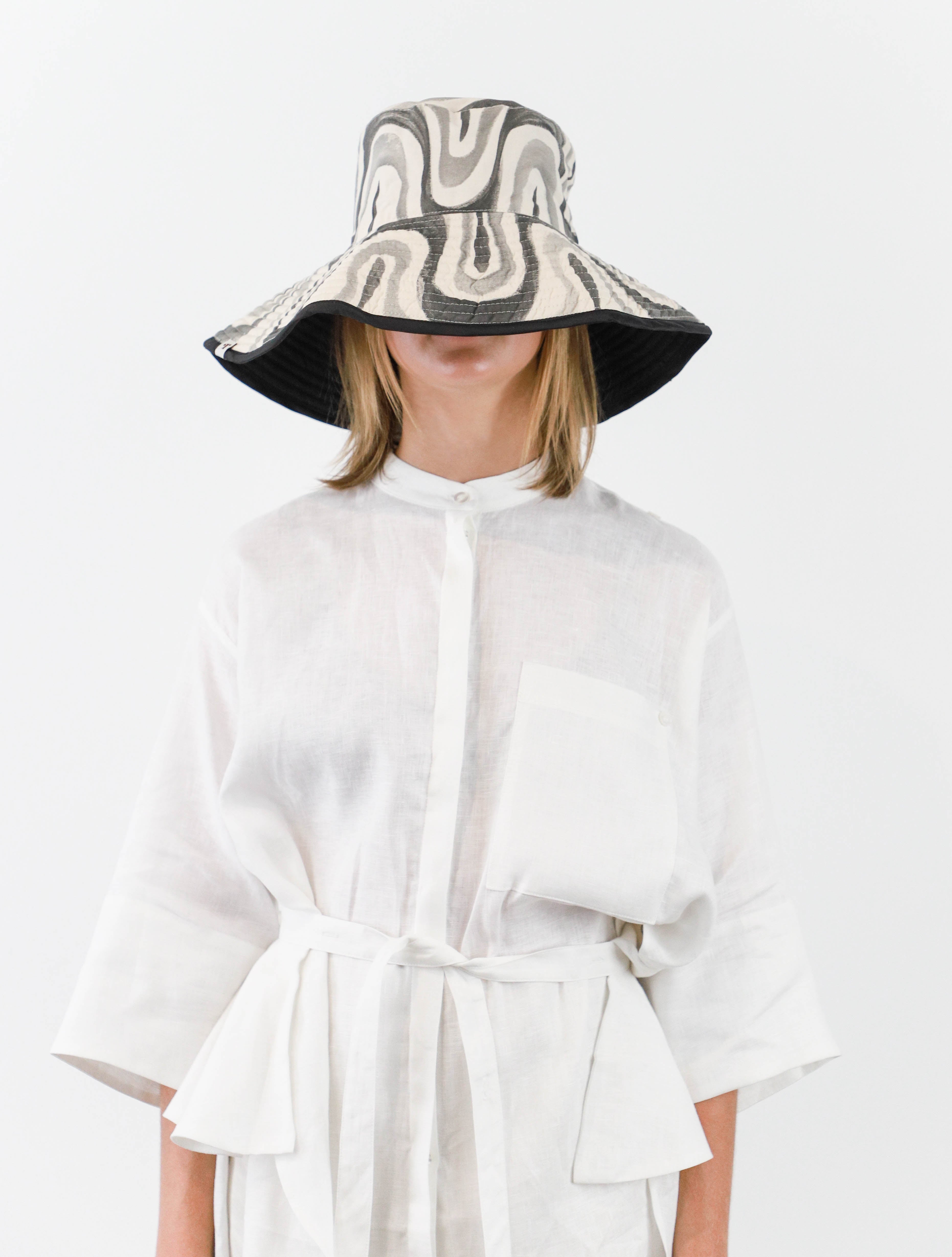 Romualda Roca bucket hat with black and white swirl pattern and black lining shown on model with brim folded up
